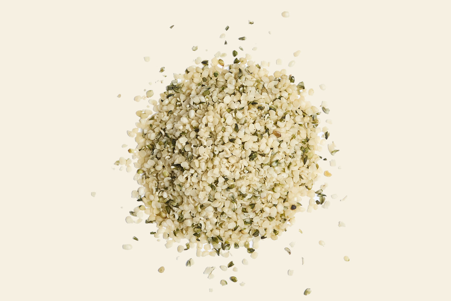 A pile of hemp seeds on a plain light background. The seeds are small, with a mix of cream and greenish hues, showcasing their natural texture and slightly irregular shapes.